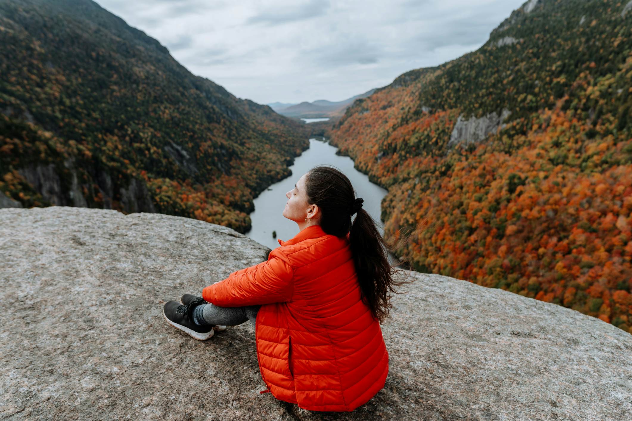 Hiking in the Adirondack Mountain Indian Head Trail in the fall
A woman sits on a rock overlooking a river and the Adirondacks mountains in the fall